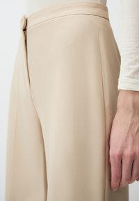Beige hoge taillebroeken, met een gladde textuur, op maat gemaakte pasvorm, ritssluiting aan de achterkant en een enkele knoopdetails.