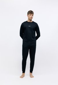 Sudadera negra de manga larga y pantalones a juego. El material es suave con un diseño ajustado. La camiseta presenta un logo blanco de "BOSS" en el pecho.