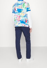 Polo tričko s krátkým rukávem v modré, zelené a růžové barvě s motivy lodí a květin; v kombinaci s námořnickými modrými kalhotami a bílými teniskami.