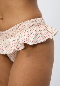 Λευκό κάτω μέρος μπικίνι με κόκκινες βούλες, με ελαστική ζώνη στη μέση με βολάν. Λείο ύφασμα με λεπτομέρειες σούρας κατά μήκος της άκρης.