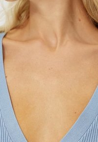 Hellblau gerippter Strickstoff mit einem tiefen V-Ausschnitt, der die glatte Haut und subtile Details in der Textur hervorhebt.