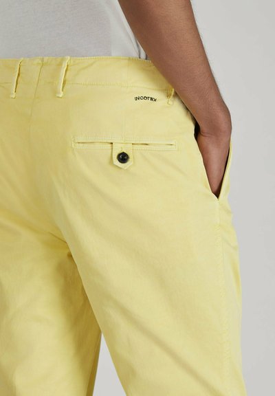 Pantaloni in cotone giallo chiaro con una tasca posteriore dotata di un bottone nero e un marchio. Tessuto liscio e vestibilità su misura.