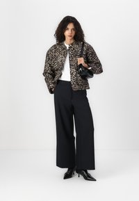 Veste bomber à imprimé léopard en tan et noir, avec un col rond et une fermeture à l'avant. Associe avec un pantalon noir à jambes larges et des escarpins pointus.
