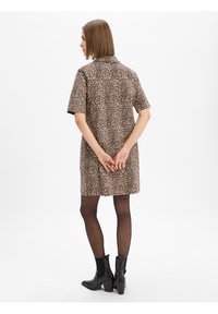Luipaardprint shirtjurk met korte mouwen, kraag en een ontspannen pasvorm. Gekleed met zwarte enkellaarsjes en doorschijnende zwarte panty.