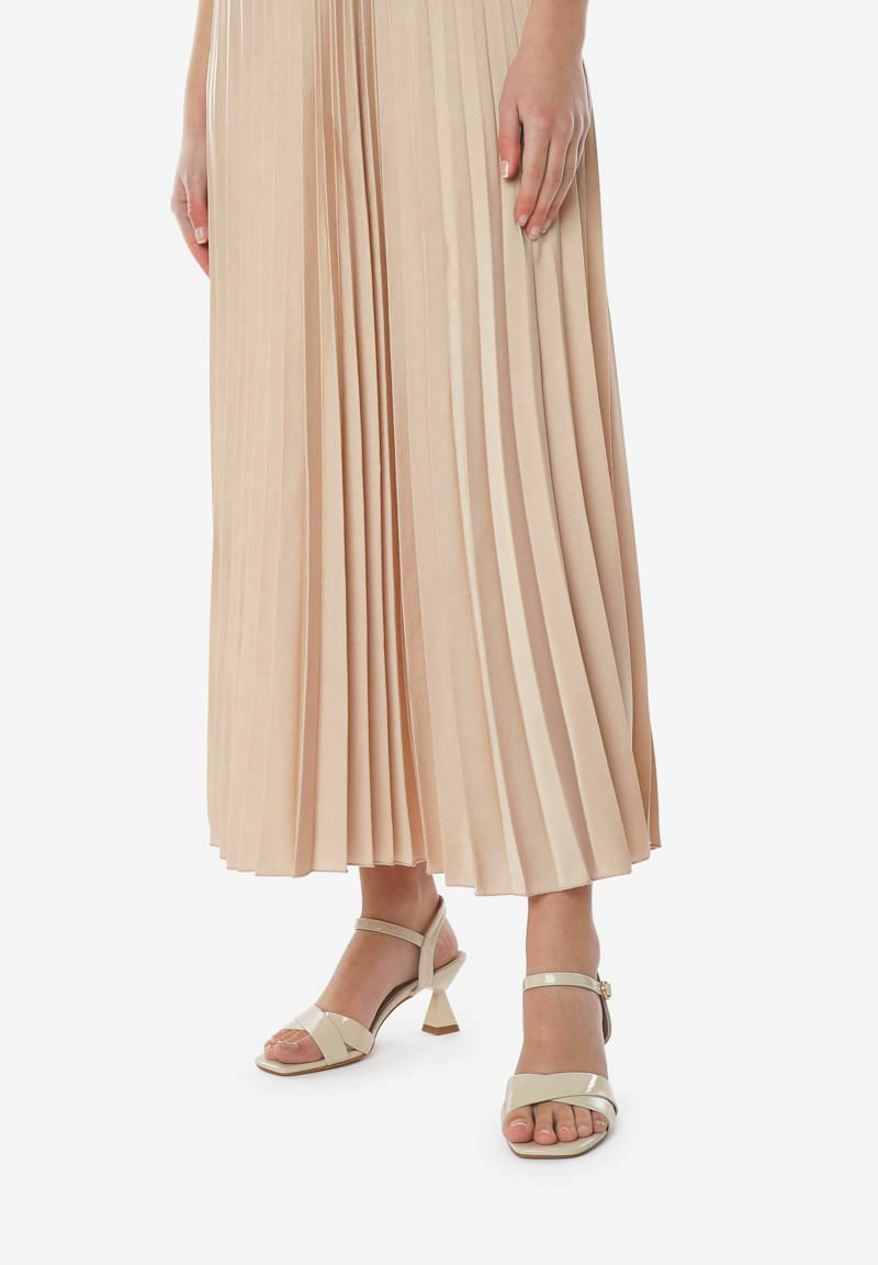 Crème kleurige haksandalen met twee brede bandjes, een blokhak en een enkelbandje. Draagstijl met een geplooide nude rok.