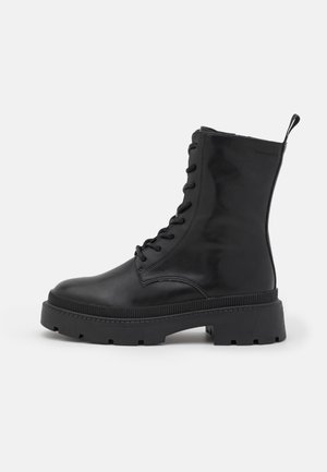 Botte de combat noire en cuir à lacets avec semelle épaisse et languette à l'arrière, vue de profil sur fond blanc.