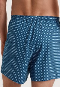 Blauwe boxer shorts met een patroon en een rasterontwerp met lichtblauwe vierkantjes. De elastische tailleband zorgt voor flexibiliteit en comfort.
