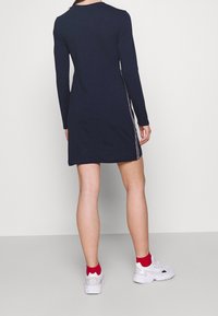 Marinblå långärmad klänning med rak skärning, med sidostråk i kontrasterande färger. Mjukt tyg med en slät yta.