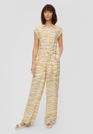 Beige en witte gestreepte jumpsuit met korte mouwen, knoopsluiting aan de voorkant, een ceintuur op de taille en wijde benen. Draagt met lichtgekleurde sandalen.