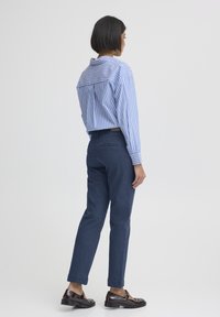 Kék-feh�ér csíkos, laza szabású ing; sötétkék nadrág; fényes fekete cipő. Simogató anyagok és klasszikus dizájnelemek.