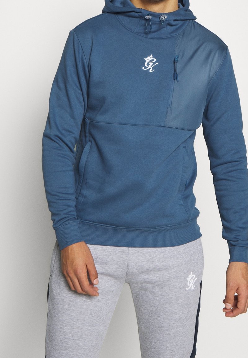 Felpa con cappuccio blu, dotata di una tasca frontale con zip, polsini elasticizzati e orlo a costine. Presenta un logo bianco sul petto e tasche laterali.