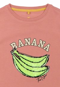 Rausvas medvilninis marškinėlis su žvilgančiu žalių bananų dizainu, viršuje esantis tekstas "BANANA" ir apačioje spausdintas "The New".