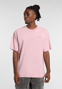 Rosa kortärmad t-shirt i bomull med runda halskant och liten logotypdetalj på bröstet. Bärs med gråbyxor.