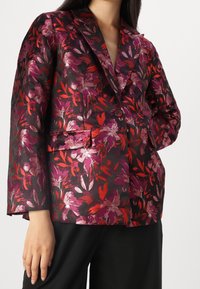 Blazer floreale nero, caratterizzato da vivaci motivi di foglie rosse e viola. Design strutturato, chiusura a un bottone e revers a punta.