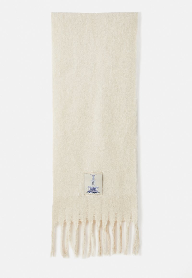 Cremefarvet uld tørklæde med frynser i enderne og et lille rektangulært mærke med et blåt krukke design nær den ene kant.