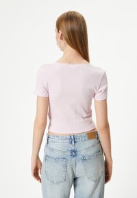 Lichtroze geribbelde top met korte mouwen en een golvende halslijn, gecombineerd met lichtblauwe high-waisted jeans met achterzakken.