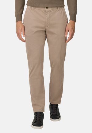 Pantaloni in cotone beige con vestibilità slim, dotati di tasche laterali e chiusura con bottone. Abbinati a sneaker nere. Texture liscia.