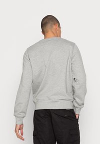 Šedá mikina, kulatý výstřih, žebrované manžety a lem, vyrobená z měkké, strukturované tkaniny. Nosená s černými cargo kalhotami.