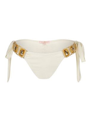 Slip bikini inferiore color crema con design a laccio sui lati, decorato con una fascia decorativa in oro e cristalli attorno alla vita. Texture liscia.