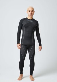 Zwarte atletische basislaagset, met een lange mouwen top van textuurstof en zilveren accenten, gecombineerd met strak aansluitende leggings en een naadloos ontwerp.