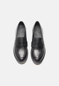 Mocassins en cuir noir avec une texture lisse, présentant une bande sur le cou-de-pied et des détails de couture subtils, conçus pour un enfilage facile.