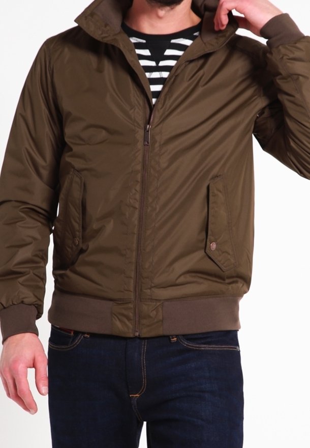 Veste bomber matelassée marron avec un col montant, une fermeture éclair, des poches latérales et des poignets côtelés ; portée avec une chemise rayée en dessous.