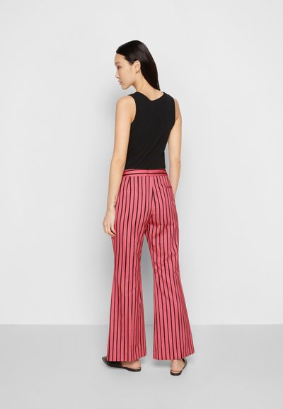 Top preto sem mangas combinado com calças cor-de-rosa de boca de sino com riscas verticais pretas. Tecido suave com um corte descontraído. Calçado simples.