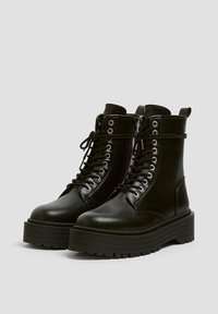 Bottes à lacets en cuir noir avec une semelle en caoutchouc épaisse, dotées d'œillets, d'une fermeture éclair latérale et d'une languette au col pour un enfilage facile.