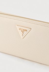 Μπεζ πορτοφόλι με υφή και χρυσό τρίγωνο λογότυπο. Διαθέτει κλείσιμο με φερμουάρ και διακριτικό ανάγλυφο μοτίβο στο υλικό.