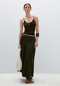 Black ribbed tank top with adjustable straps, paired with a sleek black satin maxi skirt. Accessories include a black cuff bracelet and a white textured bag.