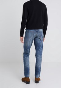 Sammafärgade blå denimjeans med en bleknad finish, med två bakfickor med sömnadsdetaljer. Kombination med en svart stickad tröja och bruna stövlar.