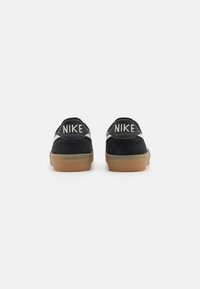 Melnas zamšādas sporta apavus ar baltām ādas akcentiem, gumijas zoli un "NIKE" logo uz papēža. Apaļa forma, zema profila dizains.