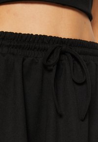 Sorte bomulls joggebukser med elastisk midje og snor. Stoffet har en myk, litt teksturert overflate.