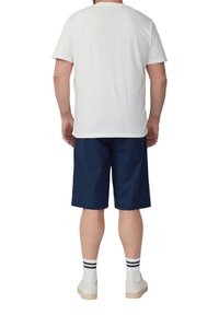 Biała bawełniana koszulka, granatowe szorty, białe trampki i w paski skarpety. Widok z tyłu ukazuje luźny krój, krótkie rękawy oraz szorty do kolan.