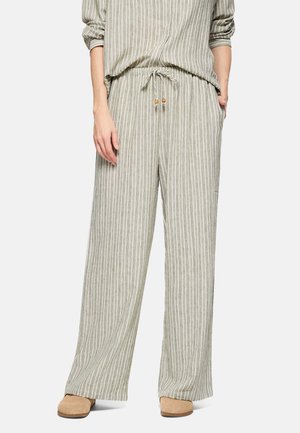 Mujer con pantalones sueltos beige con rayas verticales blancas y cintura con cordón, combinados con zapatos tipo slip-on color marrón claro.