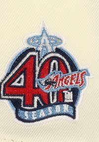 40-Jahr-Jubiläumspatch mit rot-blauer Stickerei, Text "Angels" mit einem stilisierten Logo, auf einem hellbeigen Stoffhintergrund.