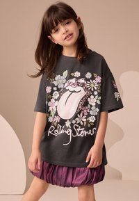 Grå bomullst-shirt med ett blommönster och en tunglogo av paljetter, kombinerad med en lila satinbubbelkjol.