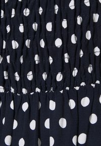 Marineblauwe stof met witte polka dots, uitgevoerd in een gestructureerd, geplooid ontwerp. Het materiaal oogt lichtgewicht en licht gekreukeld.