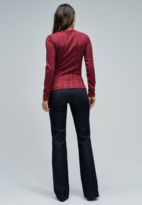 Top de manga larga burdeos con textura de canalé vertical, combinado con pantalones acampanados de mezclilla oscura. Costuras visibles y bolsillos traseros.