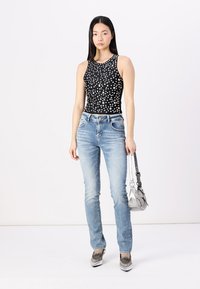 Débardeur noir avec des motifs circulaires blancs, jeans bleu clair et chaussures grises. Petit sac à main argenté avec une sangle. Style simple et moderne.