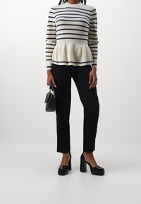 Pull rayé crème et bleu marine, modèle à base évasée, porté avec un pantalon noir et une petite pochette noire. Chaussures à talons hauts.