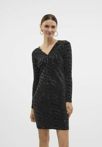 Vestido negro de manga larga con escote en V, que presenta un detalle frontal retorcido. La tela tiene una sutil textura brillante y una silueta ajustada.