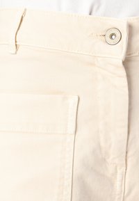 Pantaloni in denim beige chiaro con design dritto, tasca frontale e chiusura con bottone argentato in vita. Dettaglio di tessuto testurizzato visibile.