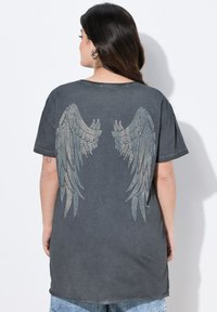 Grå bomulds t-shirt med intrikate rhinestone vinge designs på ryggen. Løs pasform med korte ærmer og rund halsudskæring.