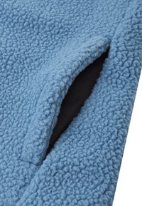 Blaue Fleecejacke mit strukturiertem Stoff und schwarzem Innenfutter, mit einer in das Design integrierten Seitentasche.
