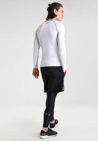 Long-sleeve white athletic top with black accents, paired with black shorts and compression leggings. Features Under Armour logo on clothing.