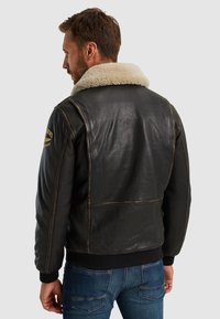 Crna kožna bomber jakna s mekim kremastim krznenim ovratnikom, rebrastim manžetama i logotipom na ramenu. Struktuirani dizajn i teksturirani završetak.