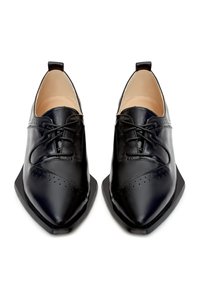 Chaussures en cuir noir à bouts pointus, avec des perforations décoratives, un laçage sur le devant et des semelles plates minimalistes.