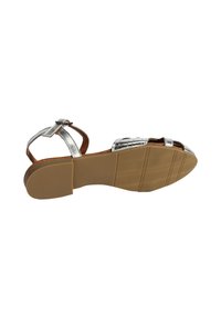 Metallic silberne Sandale mit überkreuzten Riemen, braunen Akzenten und flacher Gummisohle. Offene Zehenpartie mit strukturiertem Grip auf der Unterseite.