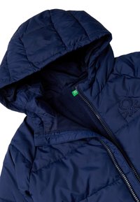 Giacca puffo blu navy con design trapuntato, cappuccio e rivestimento in pile. Presenta una zip frontale e un logo ricamato sul petto.